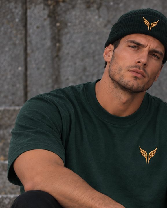 A man in a pine green beanie and a matching t-shirt, the gold wings on the turn-up of the hat.
