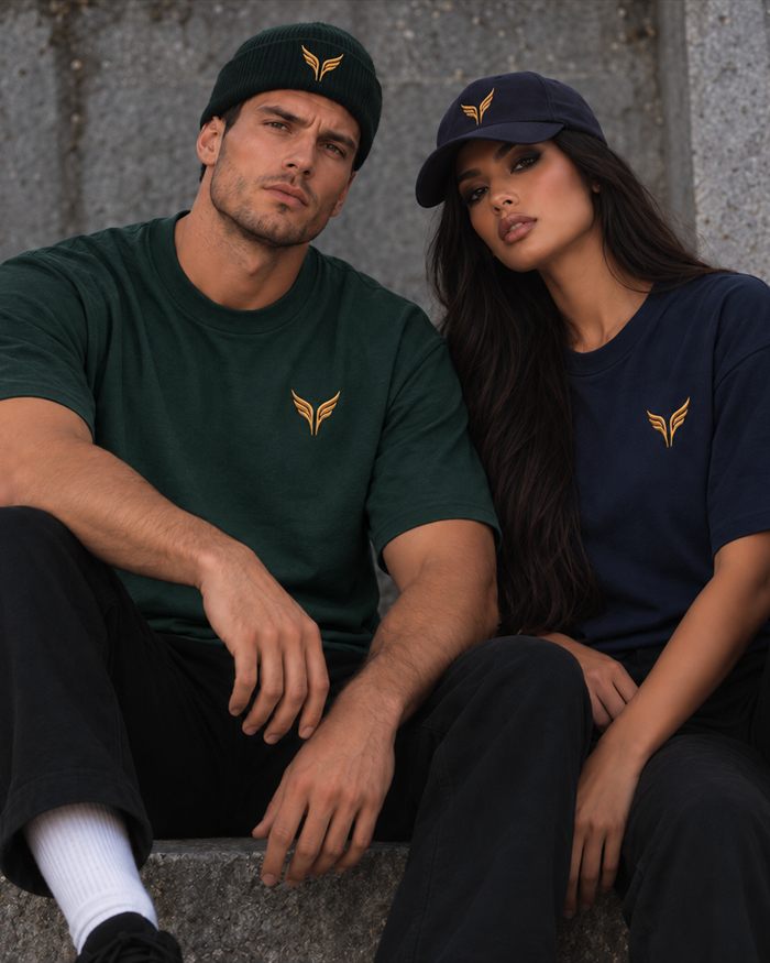 A man in a pine green t-shirt and beanie sitting beside a woman in a midnight blue t-shirt and cap.
