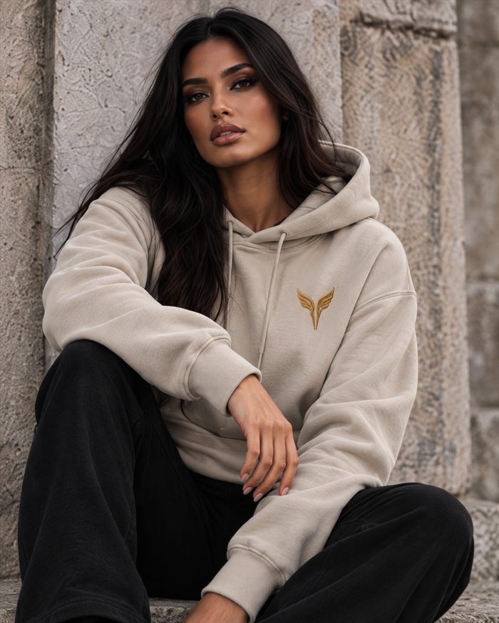 A woman in a bone hooded sweatshirt with the gold wings on the left chest.