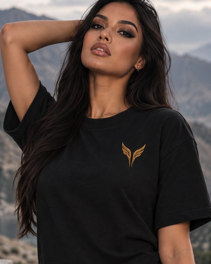 A woman in a black t-shirt with the gold wings on the left chest, mountains behind her.